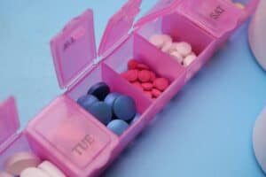 Pink pill organizer with colorful tablets arranged for weekly medication management.