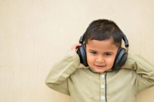Young boy enjoying music with headphones, wearing beige shirt against a neutral background.