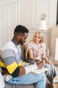 A caring volunteer assists an elderly woman in monitoring her blood pressure indoors.