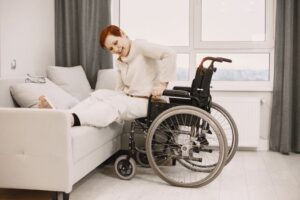 A woman with dyed short hair smiles while transitioning from a wheelchair to a couch.