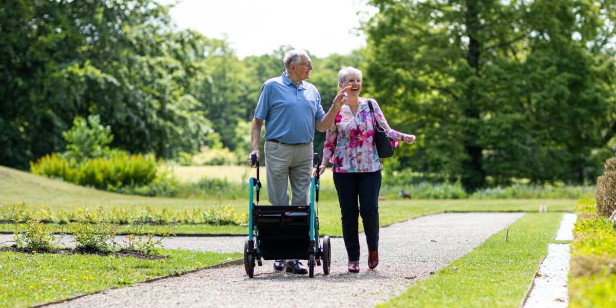 Senior couple walking in a park with a walker, enjoying a sunny day outdoors.