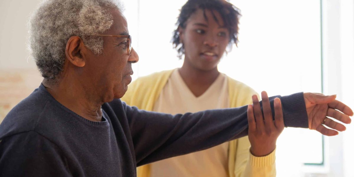 A caregiver helps an elderly man with arm exercises in a warm and caring environment.